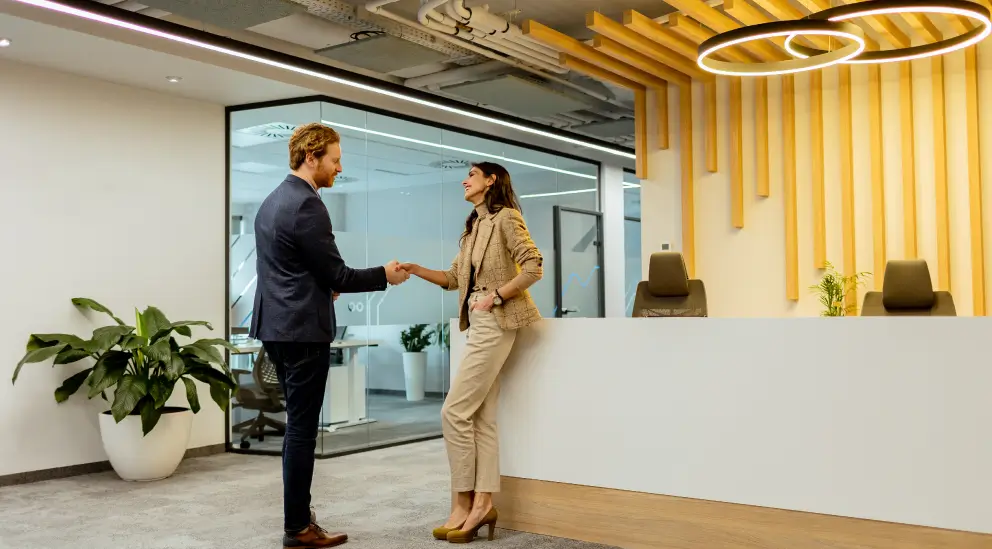 Colleagues shaking hands at a modern reception desk with wood slat ceiling