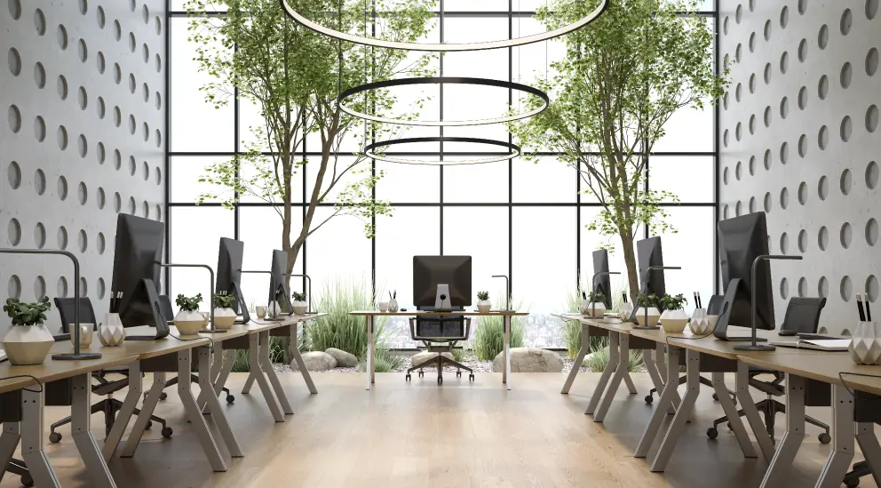 Office workstations surrounded by tall potted trees and floor-to-ceiling windows